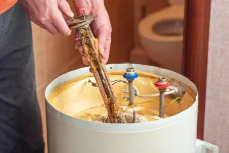 A plumber pulls a corroded heating element out of a water heater.