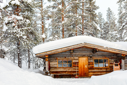 A low log cabin surrounded by trees and covered in snow.